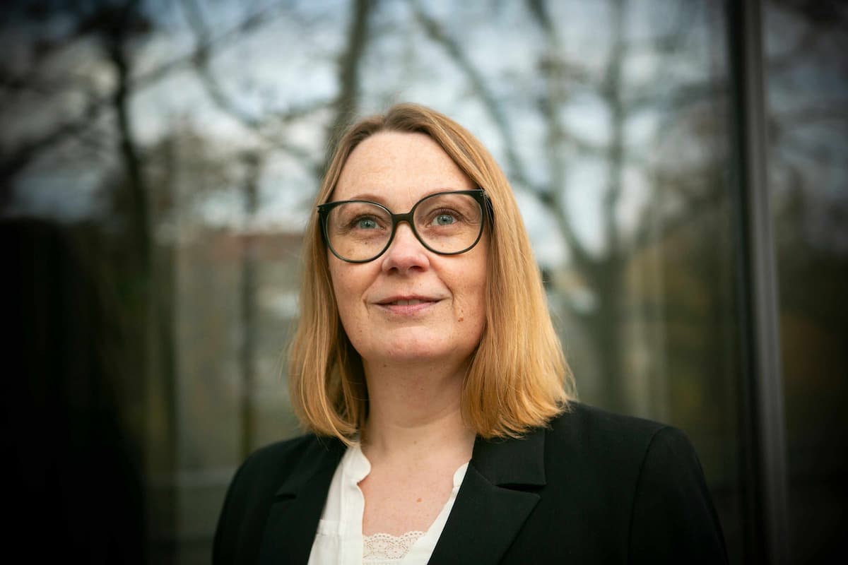 placeholder-image Lene Stampe, der arbejder med konflikthåndtering for virksomheder. Hun står foran store vinduer, hvor en skov spejler sig