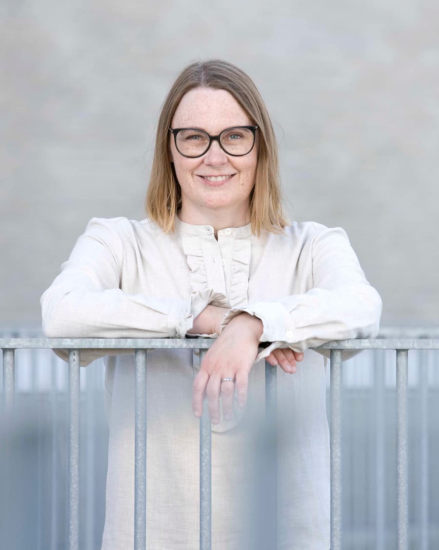 blog-billede-pladsholder Lene Stampe står med armene hvilene på et rækværk og smiler til dig