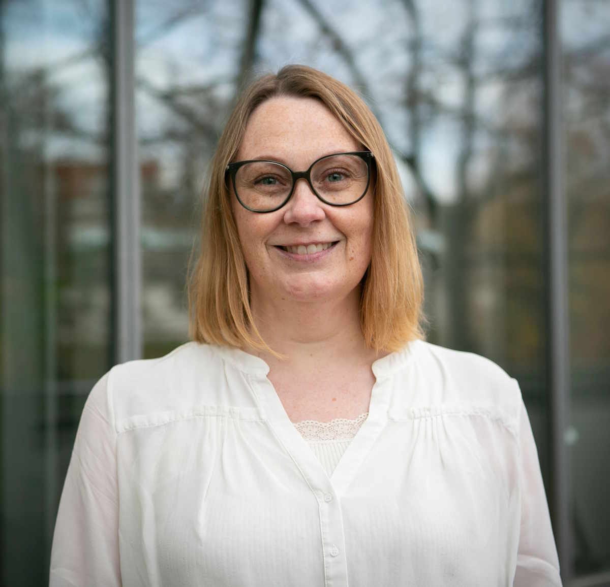 blog-billede-pladsholder Lene Stampe står foran en rude, hvor træer reflekteres